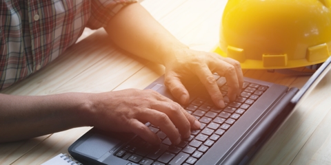 Person using laptop for working with yellow helmet on table.