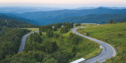 Large tractor trailer driving down the highway surrounded by trees