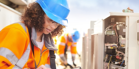 Female electrician with aircon unit using a tablet.