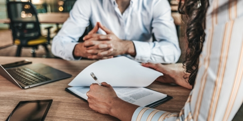 Two people sitting at a table with a woman reviewing and signing documents
