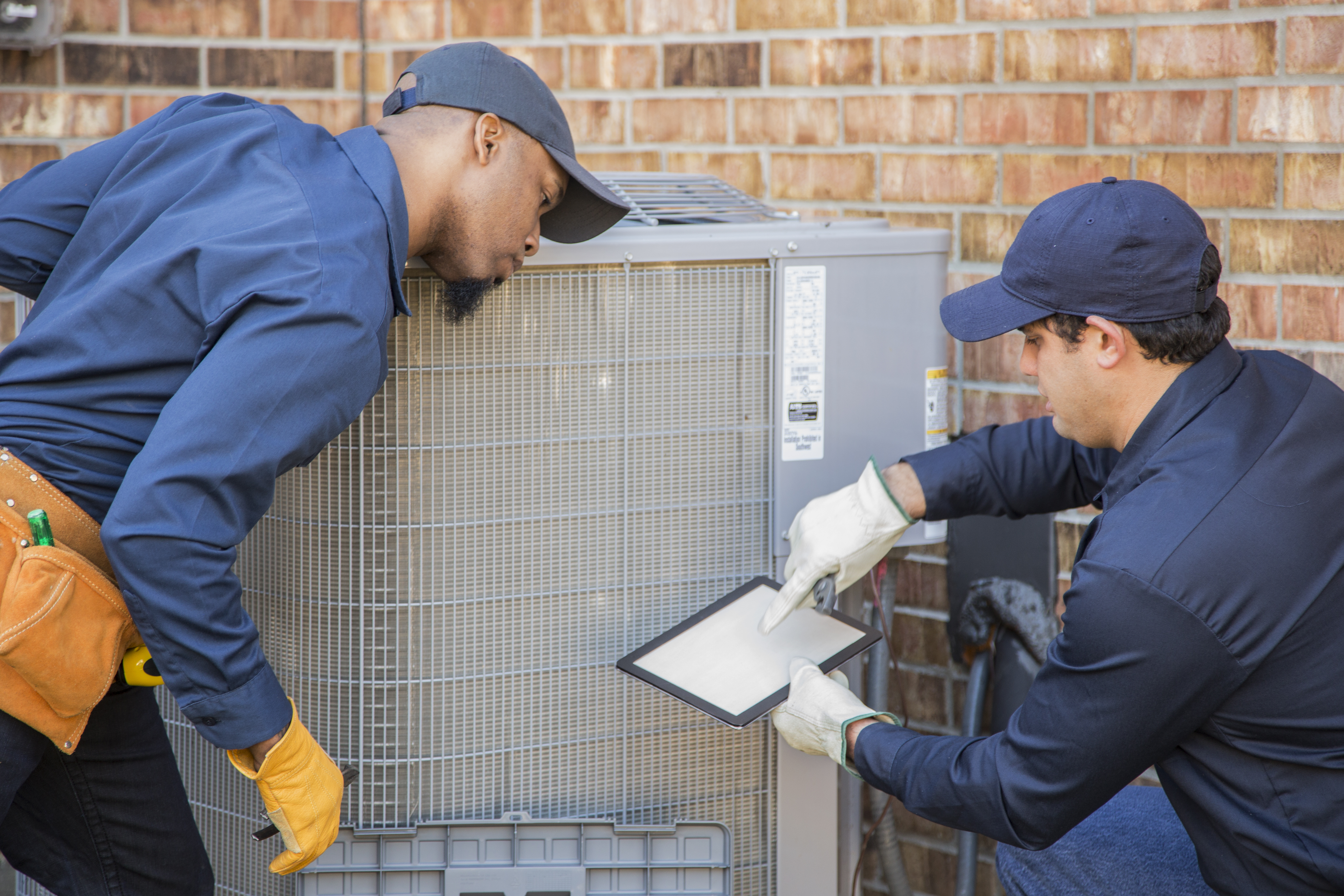 two HVAC technicians working on an AC unit