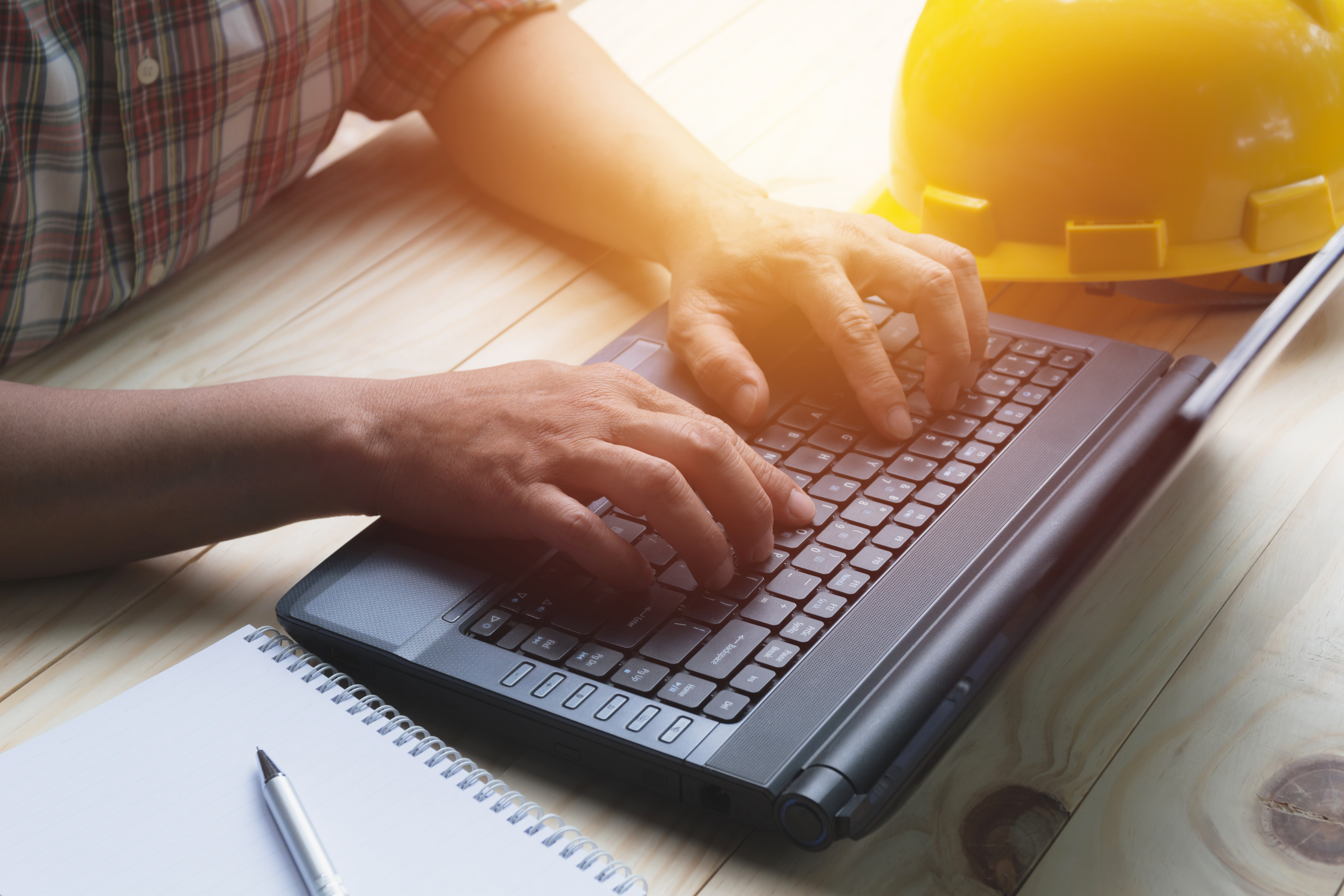Person using laptop for working with yellow helmet on table.