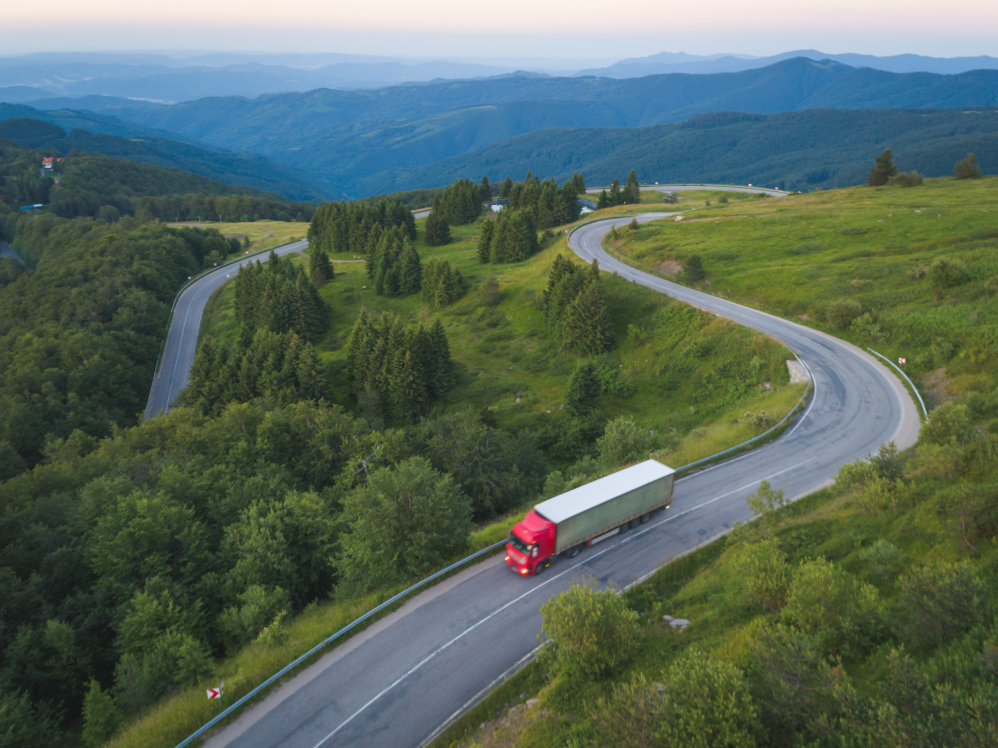 Large tractor trailer driving down the highway surrounded by trees