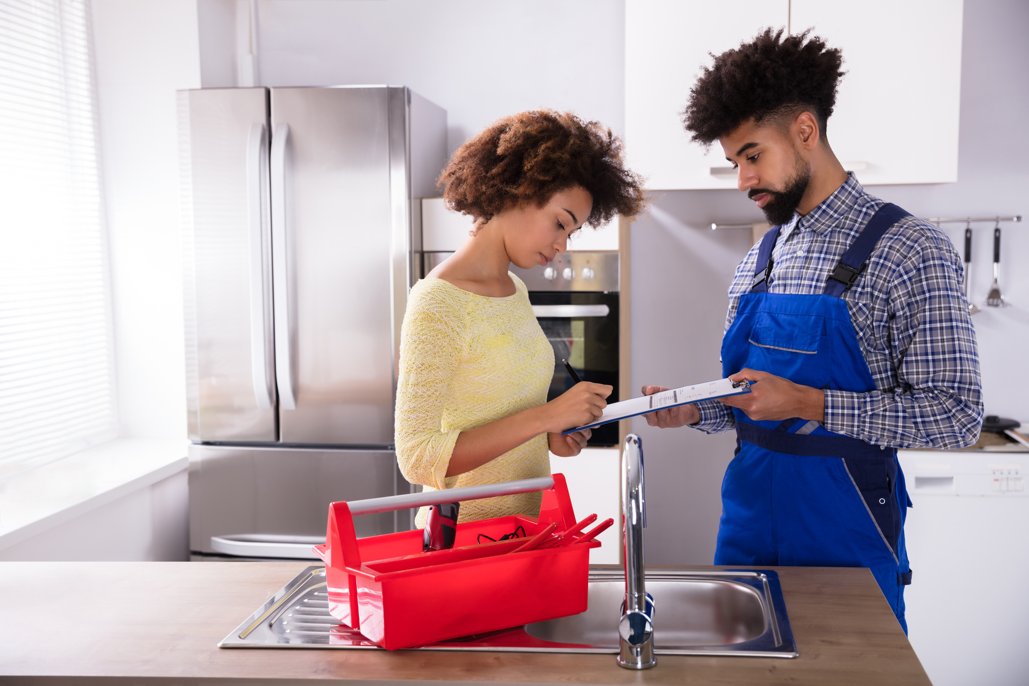 Woman Signing Plumbing Invoice In Kitchen